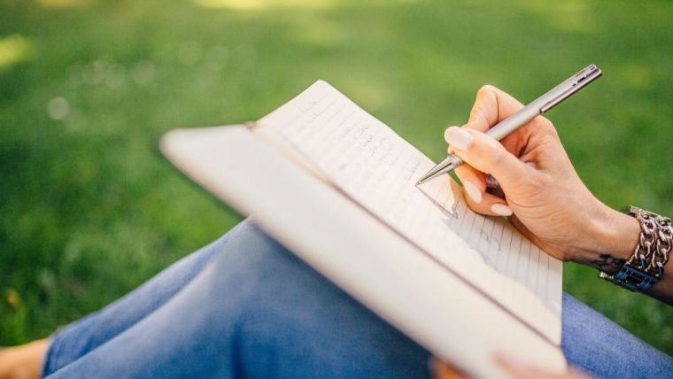 Woman sitting on the grass writing in a journal