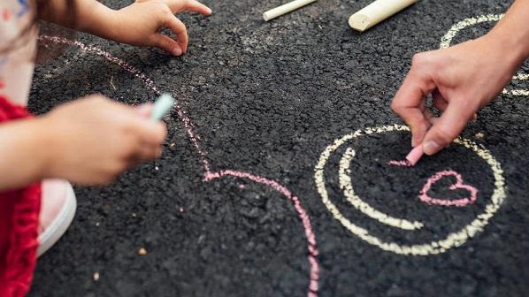 Children drawing smiley faces with chalk on a tarmac playground floor
