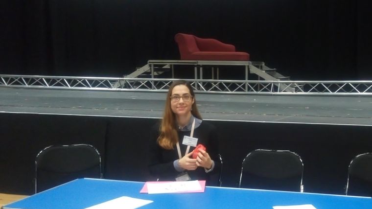 Dr Sophia Malandraki-Miller sat at a table holding a prosthetic heart in front of a stage at Oxford High School