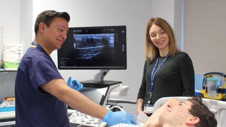 Doctors smiling to a patient while doing some scan. There is a screen showing what they are checking.