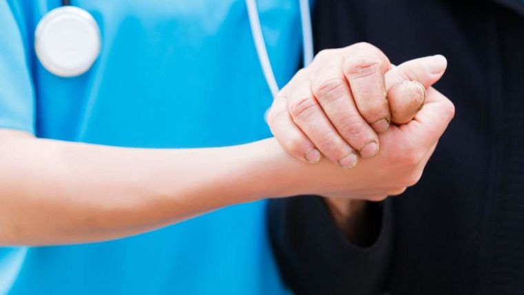 Nurse or doctor holding elderly patient's hand with care