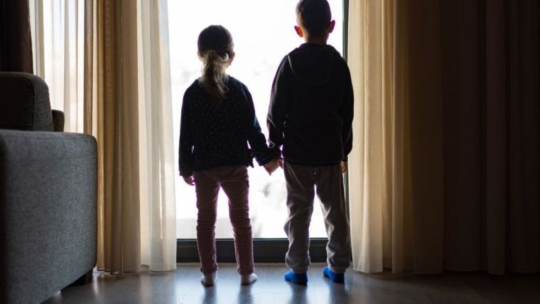 Two children holding hands looking out of a window