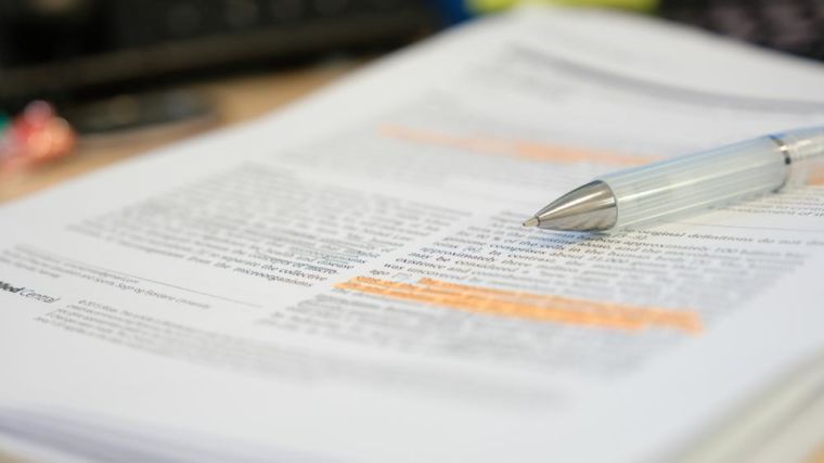 Stack of academic papers with text highlighted and a pen resting on top