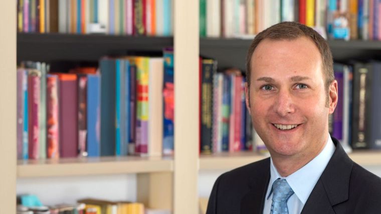 A portrait photograph of Prof Michael Kidd in front of a bookshelf