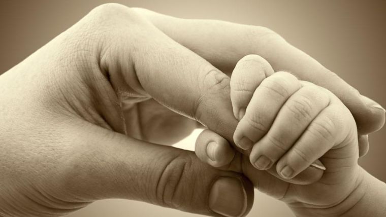 Hand of a mother and a baby grabbing her finger in sepia color